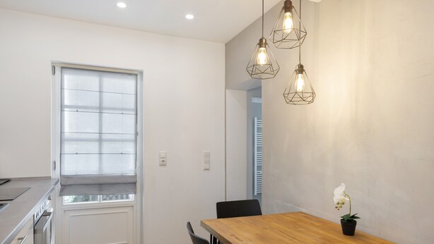 Una cocina moderna con una mesa de comedor de madera, luces colgantes y una orquídea en maceta.