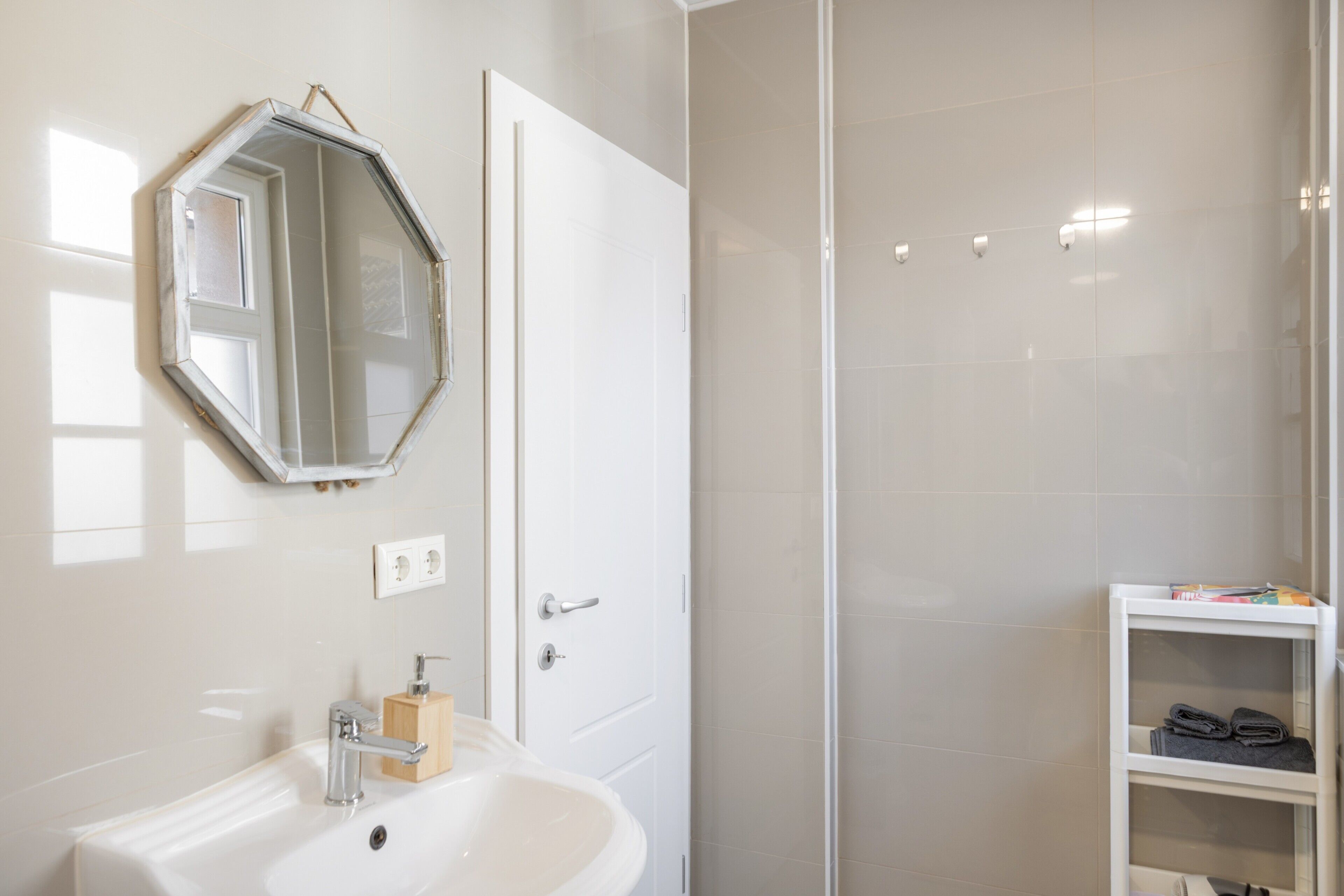 A bathroom with a white sink, a mirror, a door, and a shower area.