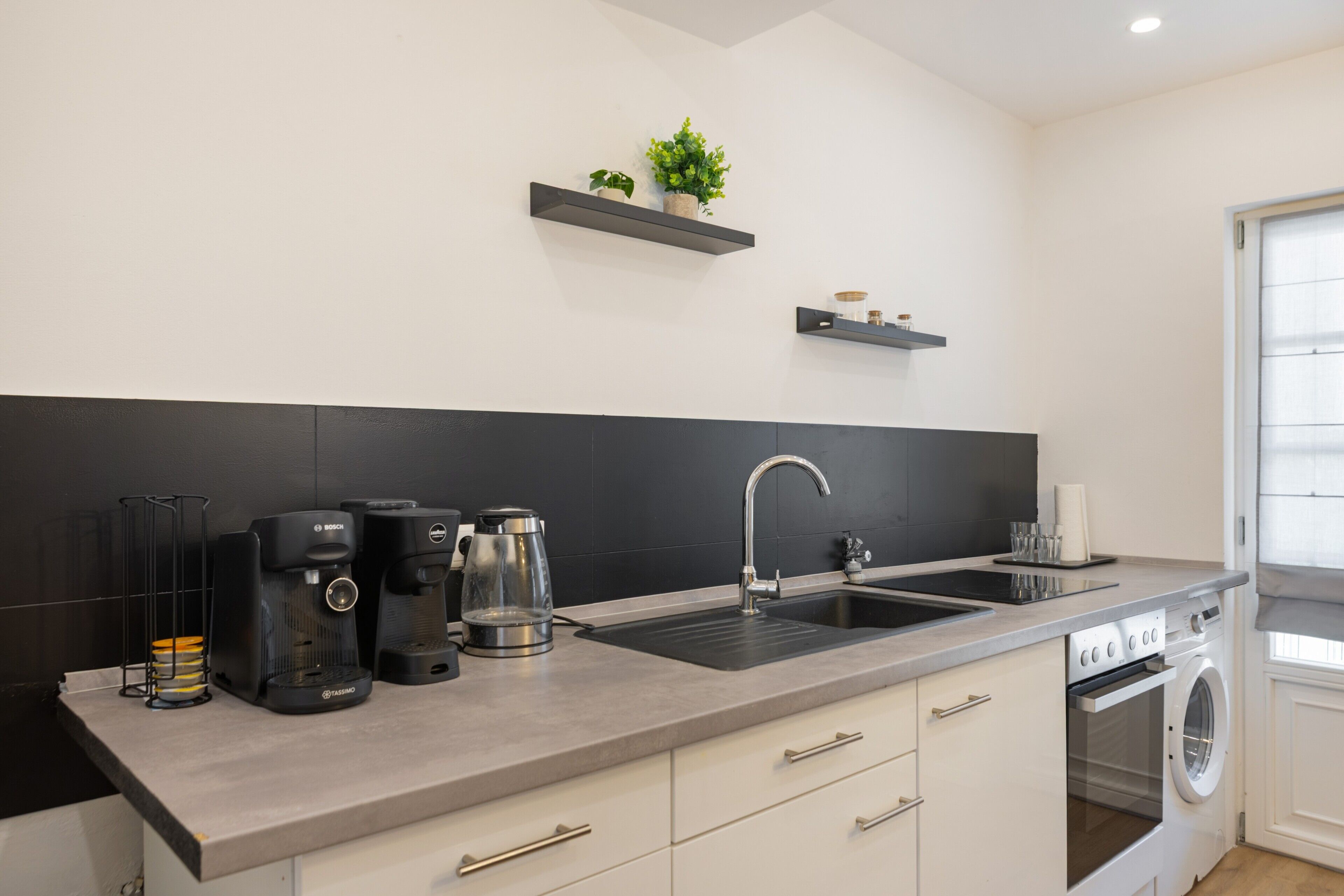 Eine moderne Küche mit Waschmaschine, Kaffeemaschine und Spüle.