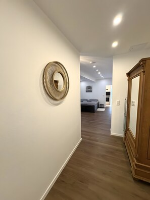 Un pasillo con piso de madera, un espejo grande y una puerta a la derecha.