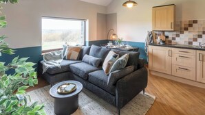 A cozy living area with a sectional sofa, a coffee table, and a view of the outdoors. - Black Bird Cottage (Gaerwen)