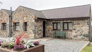A stone building with a sloped roof, a bench, and a gravel driveway. - Black Bird Cottage (Gaerwen)