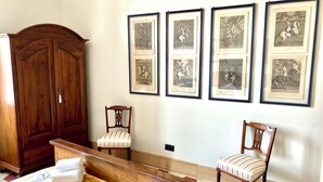 Quarto de hotel com um grande armário de madeira, uma cama com colcha amarela, duas poltronas estofadas e uma parede decorada com gravuras de cavalos.