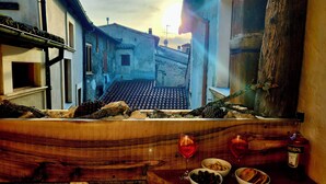 Uma mesa de madeira rústica com vista para uma rua estreita, uma garrafa de Aperol e tigelas com petiscos.