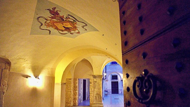 Um corredor interno com tetos em arco, piso ladrilhado e um mural decorativo no teto.