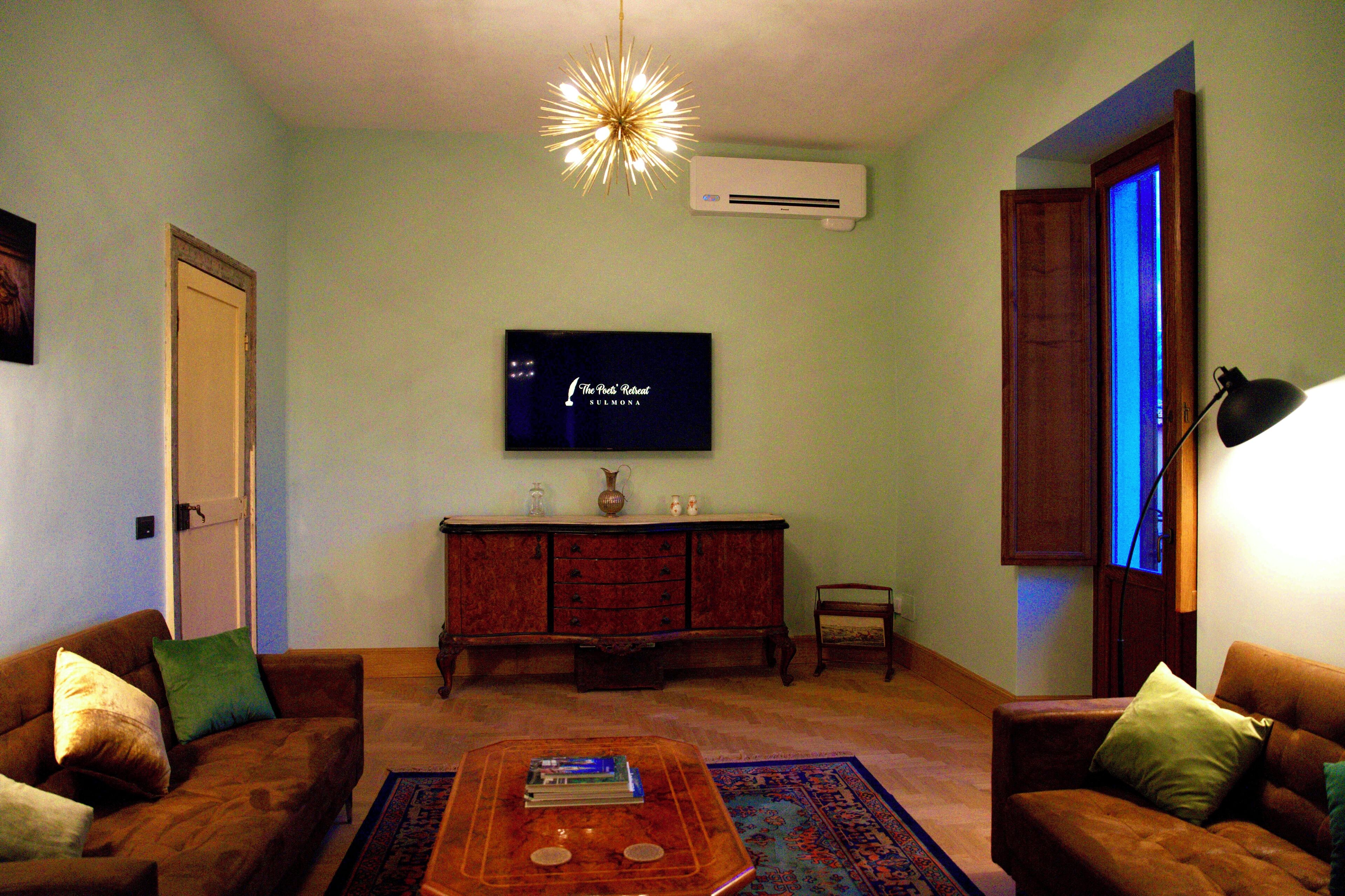 A living room with a flat-screen TV, a wooden cabinet, two sofas, a coffee table, and a patterned rug.
