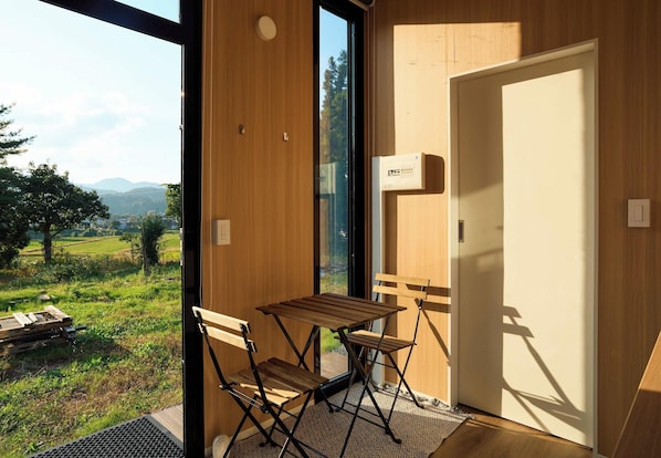 A room with a large window, a wooden table, two chairs, and a door.