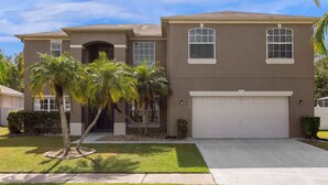 A two-story house with a garage, palm trees, and a well-maintained lawn. - Upstay Home w Pool Hot Tub Patio - Pet Friendly (Kissimmee)