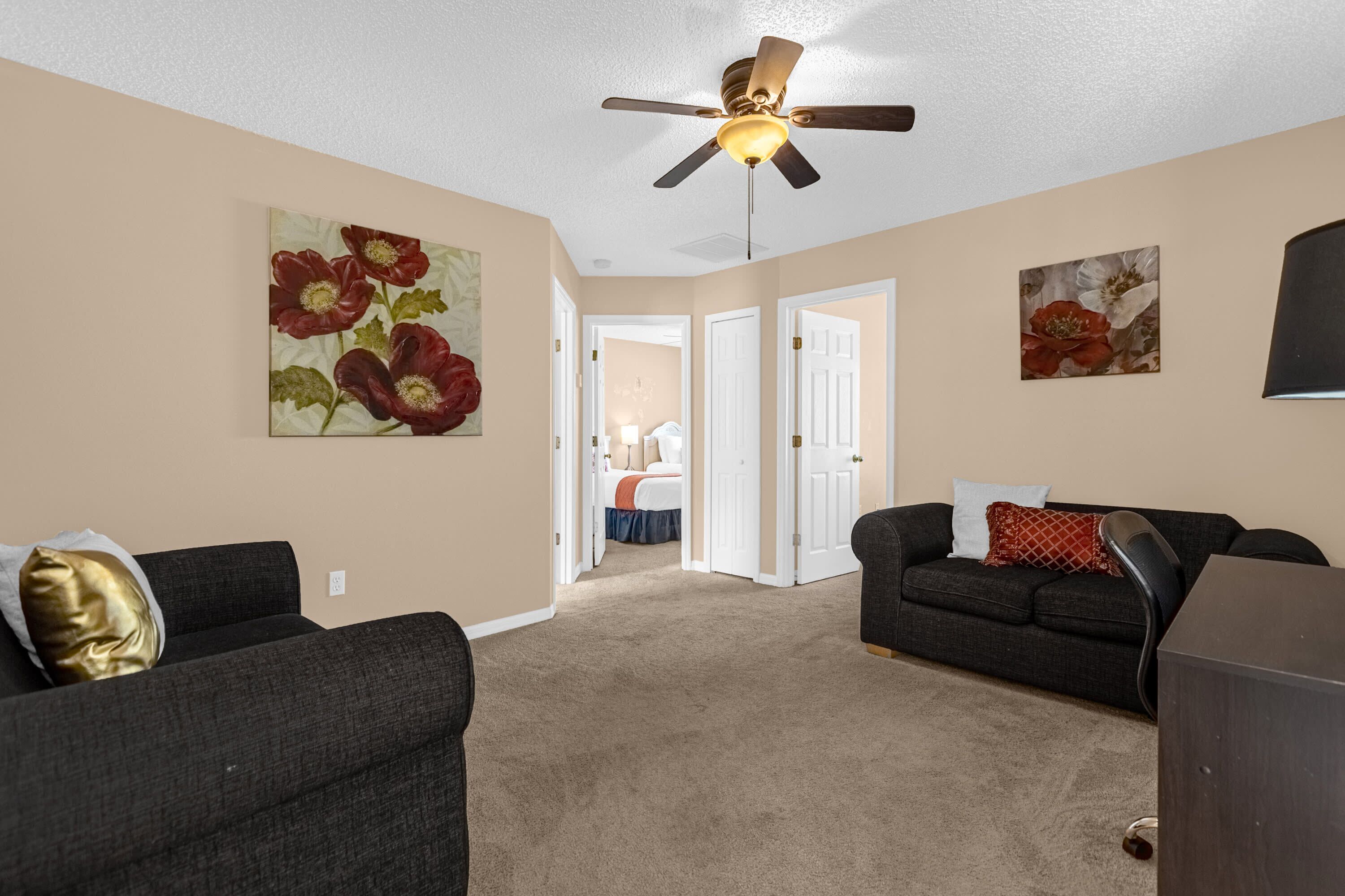 A living room with two dark sofas, a ceiling fan, and artwork on the walls.