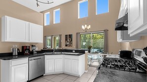 A modern kitchen with white cabinets, a black countertop, a built-in dishwasher, a gas stove, and a large window providing natural light. - Upstay Home w Pool Hot Tub Patio - Pet Friendly (Kissimmee)