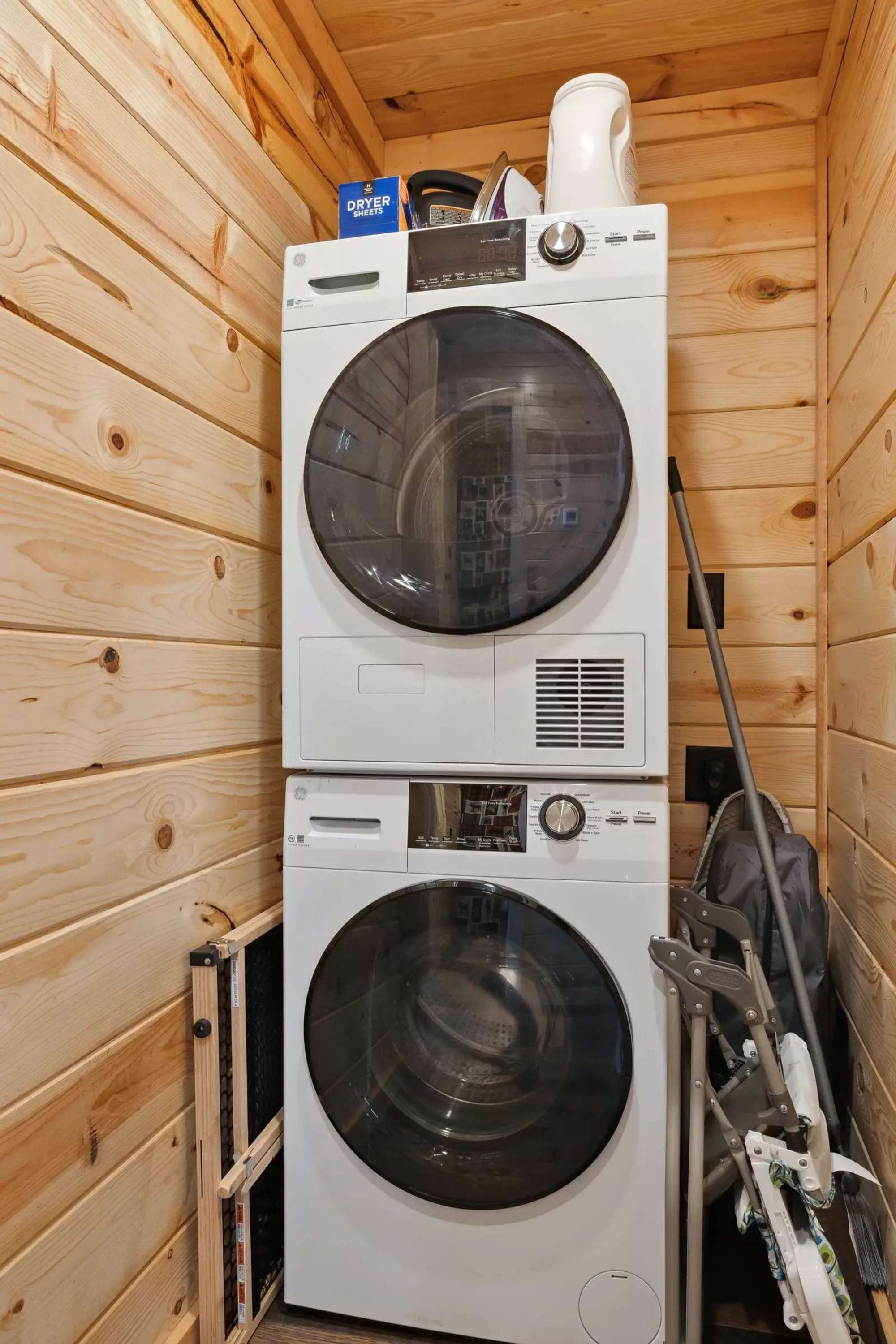 Een gestapelde wasmachine en droger in een houten blokhut met houten vloer en wanden.