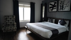 Quarto com uma cama grande, uma cadeira e duas janelas com cortinas.