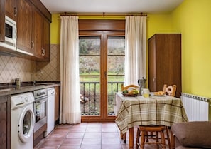 A kitchen with a washing machine, a dining table with a tablecloth, and a view through a glass door to an outdoor area. - Rural Apartments La Viña (Apartment number 7) (Cangas de Onis)