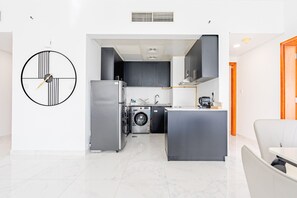 A modern kitchen with a central island, built-in appliances, and a large wall clock. - Lake-View Apartment Near City Centre Me’aisem Mall, Mins from Autodrome and ICC Cricket Stadium (Dubai)