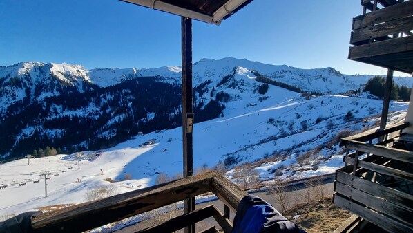 A wooden deck overlooking a snow-covered mountain landscape with ski slopes and a clear blue sky.