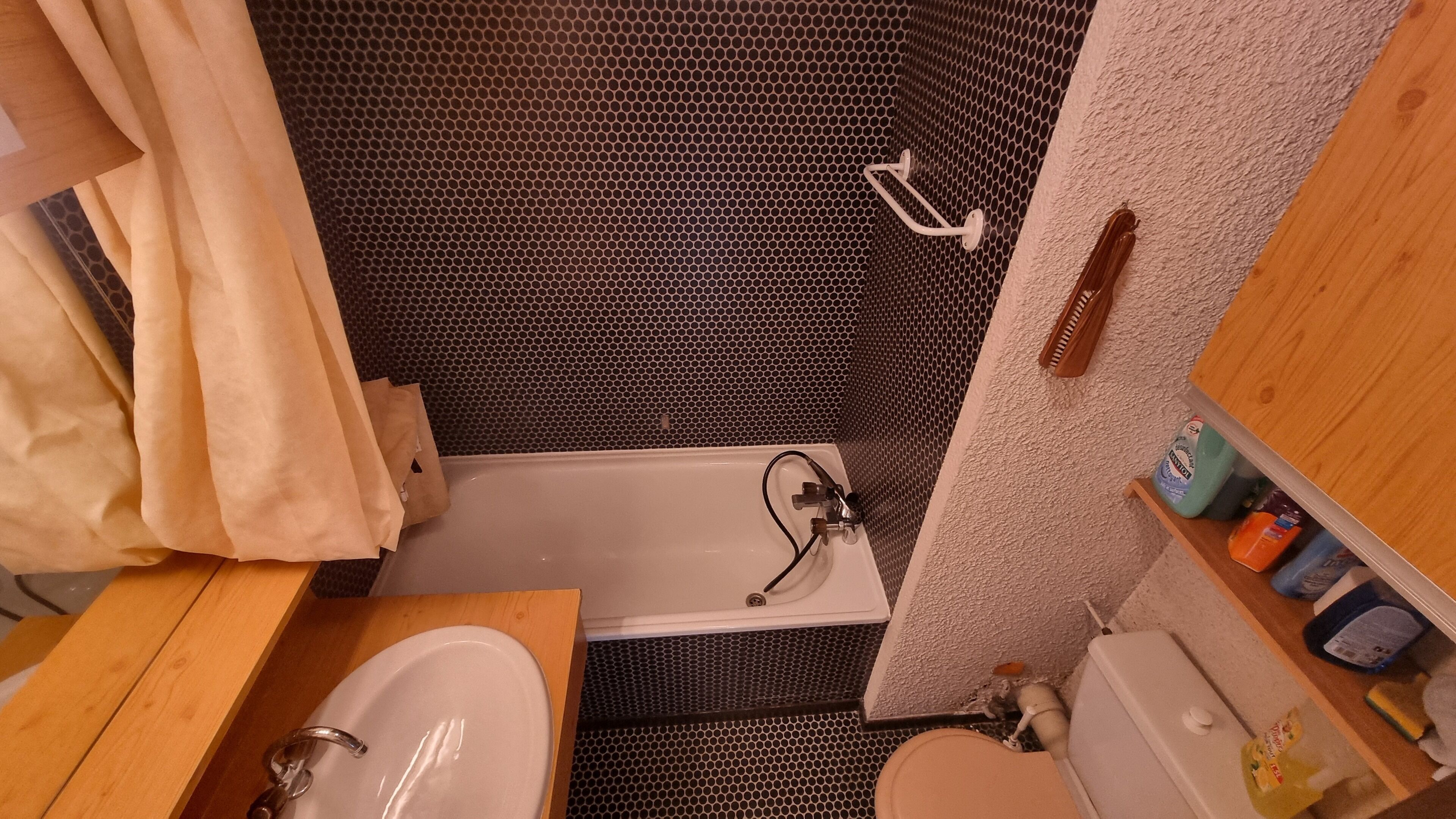 Une petite salle de bain avec un lavabo blanc, une baignoire et un espace douche doté d’un carrelage à motifs noir et blanc.