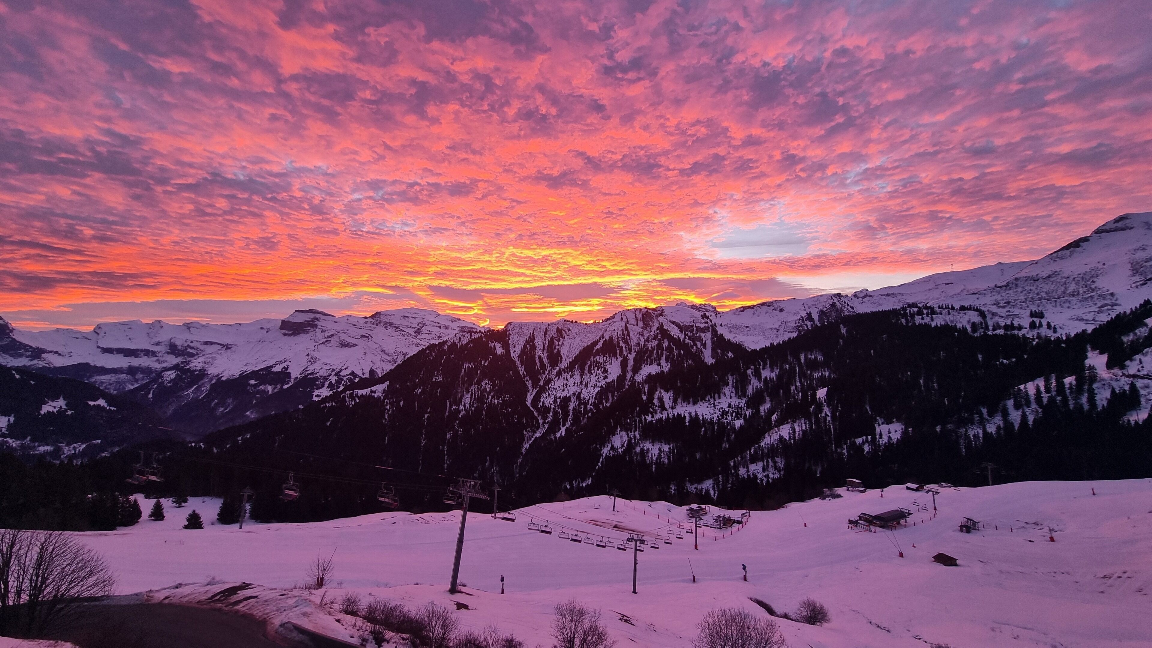 Un paysage de montagne enneigé, avec un télésiège et un coucher de soleil.