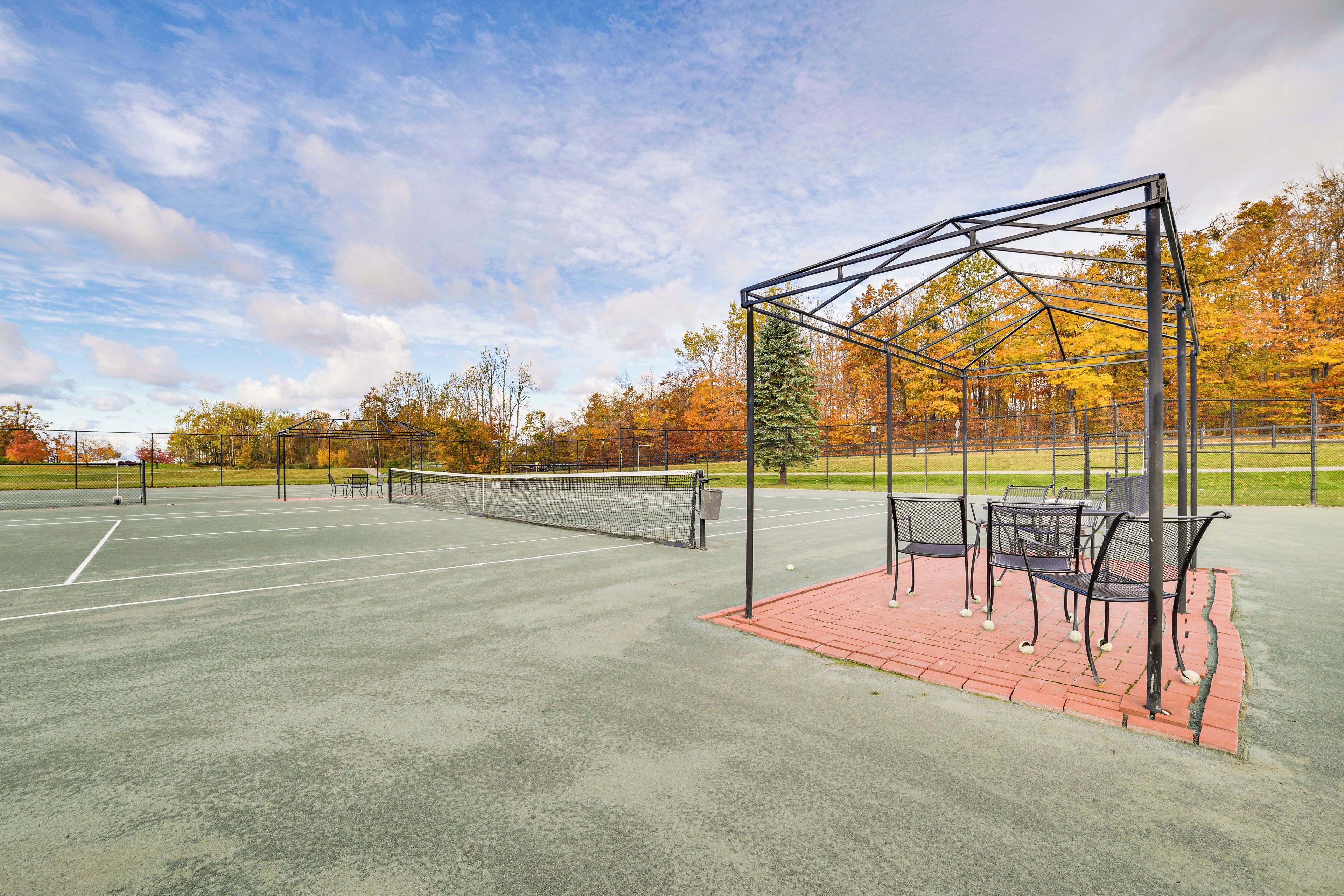 Een tennisbaan buiten met een metalen paviljoen en zitgedeelte.