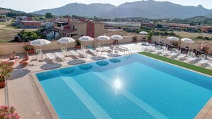 Une grande piscine entourée de bâtiments et de montagnes, avec des chaises longues et des parasols.