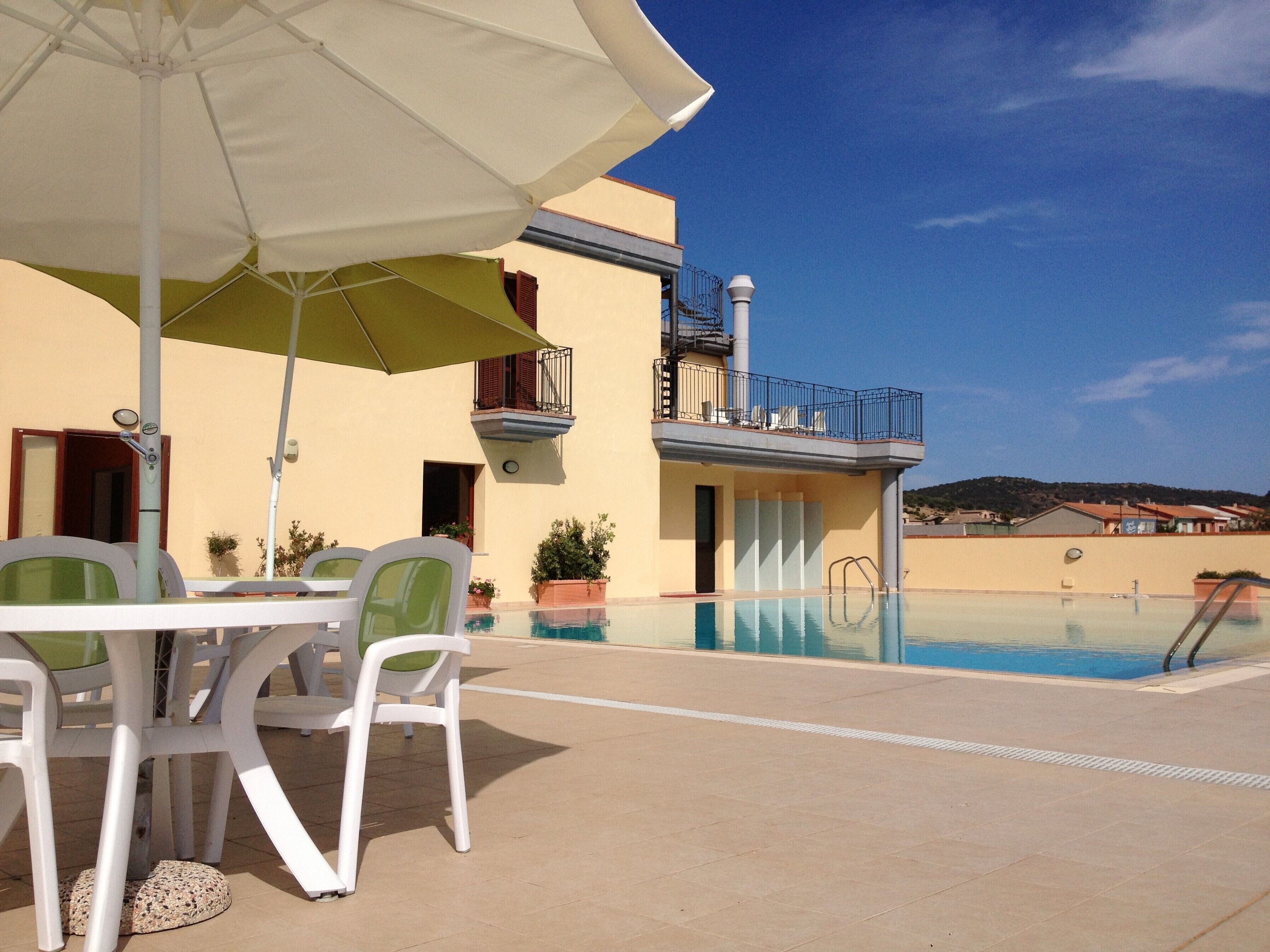 A poolside area with a table and chairs, a pool, and a building with a balcony.