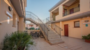 Un bâtiment avec un escalier menant à un deuxième étage, des plantes en pot et des vélos garés à l’extérieur.