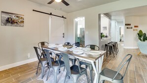 A dining area with a long table set for six, surrounded by metal chairs, a ceiling fan, and a painting on the wall.