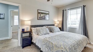 A bedroom with a bed, two bedside tables, a ceiling fan, a window with curtains, and a wall-mounted picture.