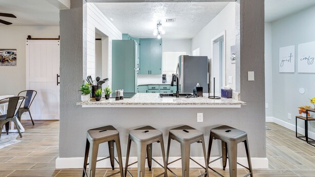 A modern kitchen with a central island, bar stools, and a view into the dining area.