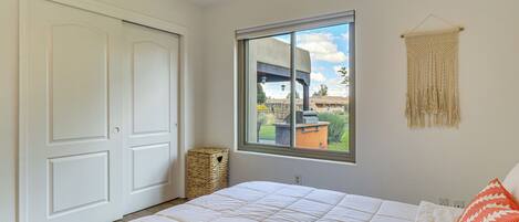 A bedroom with a large bed, a window with a view of the outdoors, a woven basket, and a macrame wall hanging.