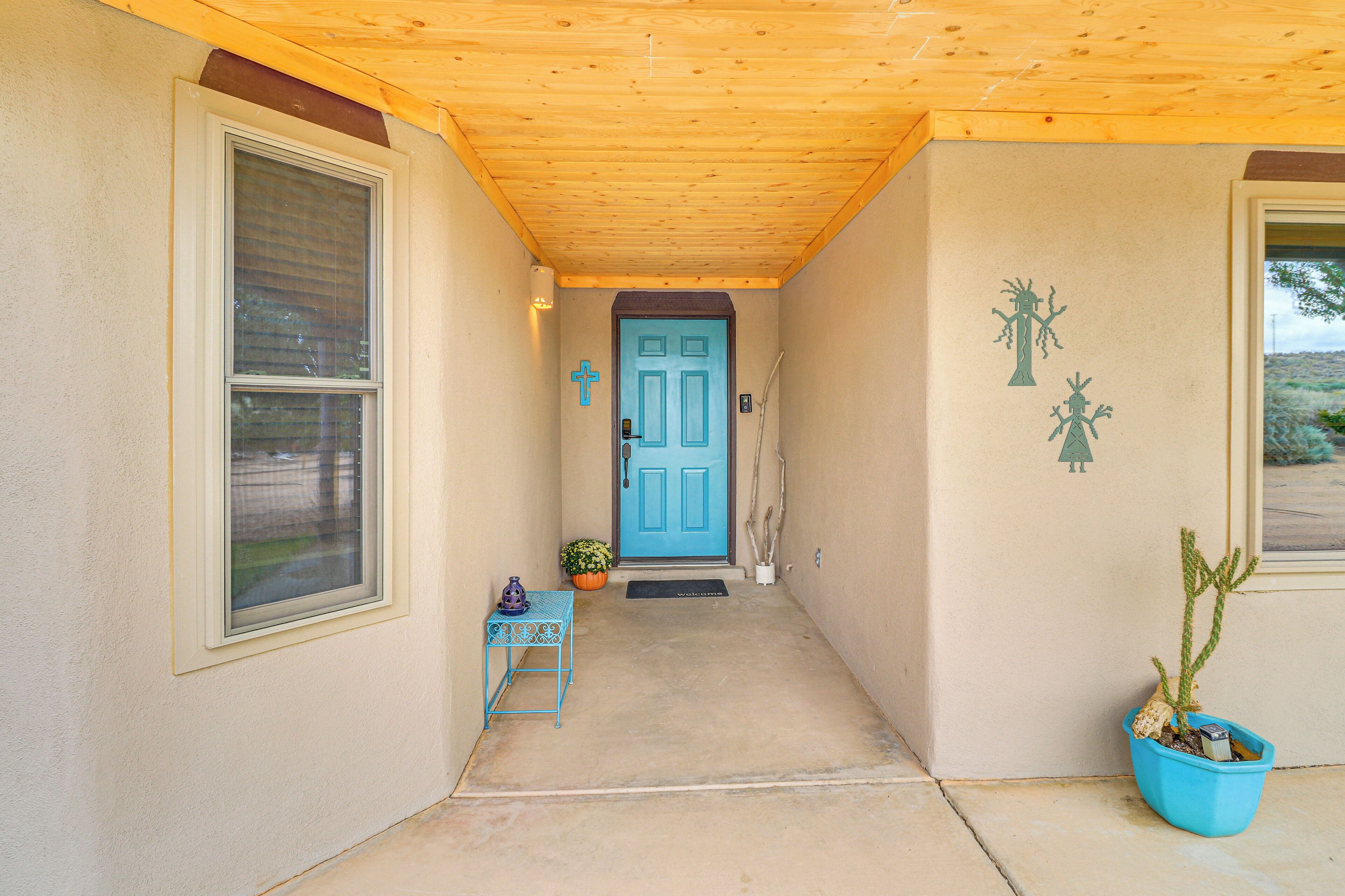 Una entrada de casa con una puerta azul, una pequeña mesa con una planta y un cactus en maceta junto a la puerta.