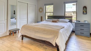 A bedroom with a wooden bed, a bedside table, a bench, and a window with a view of the outdoors.