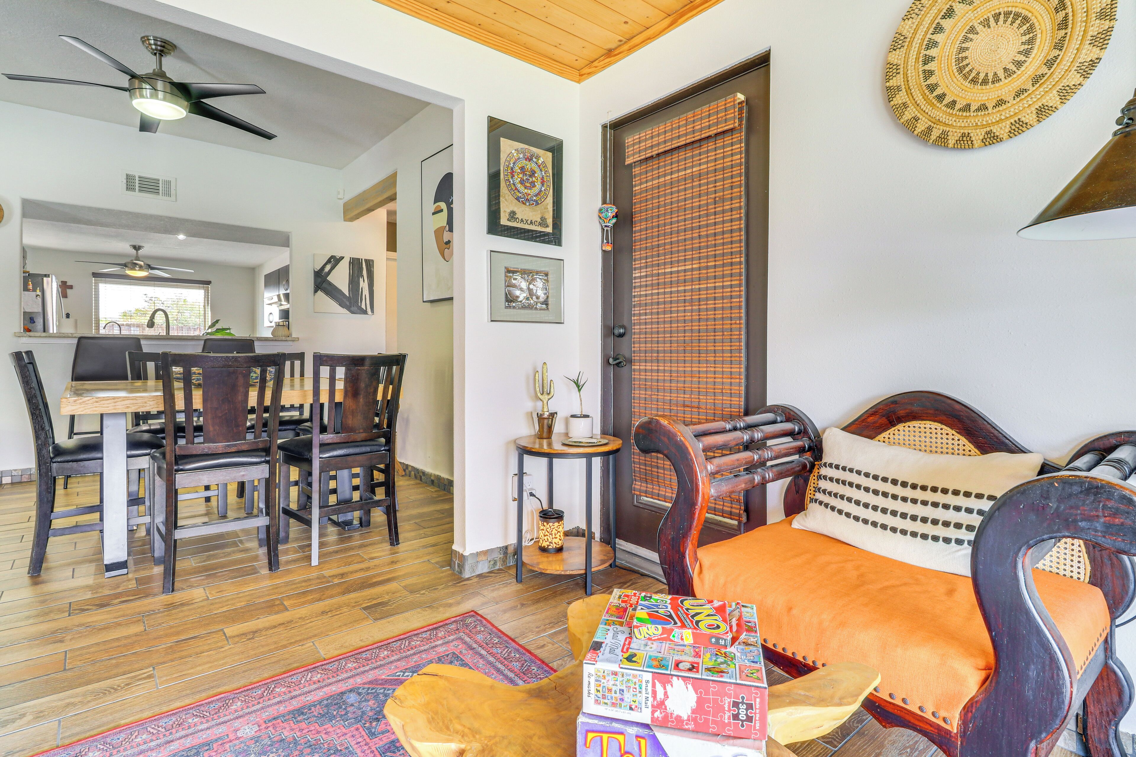 A room with a bed, a dining table with chairs, a ceiling fan, and a door with a woven curtain.