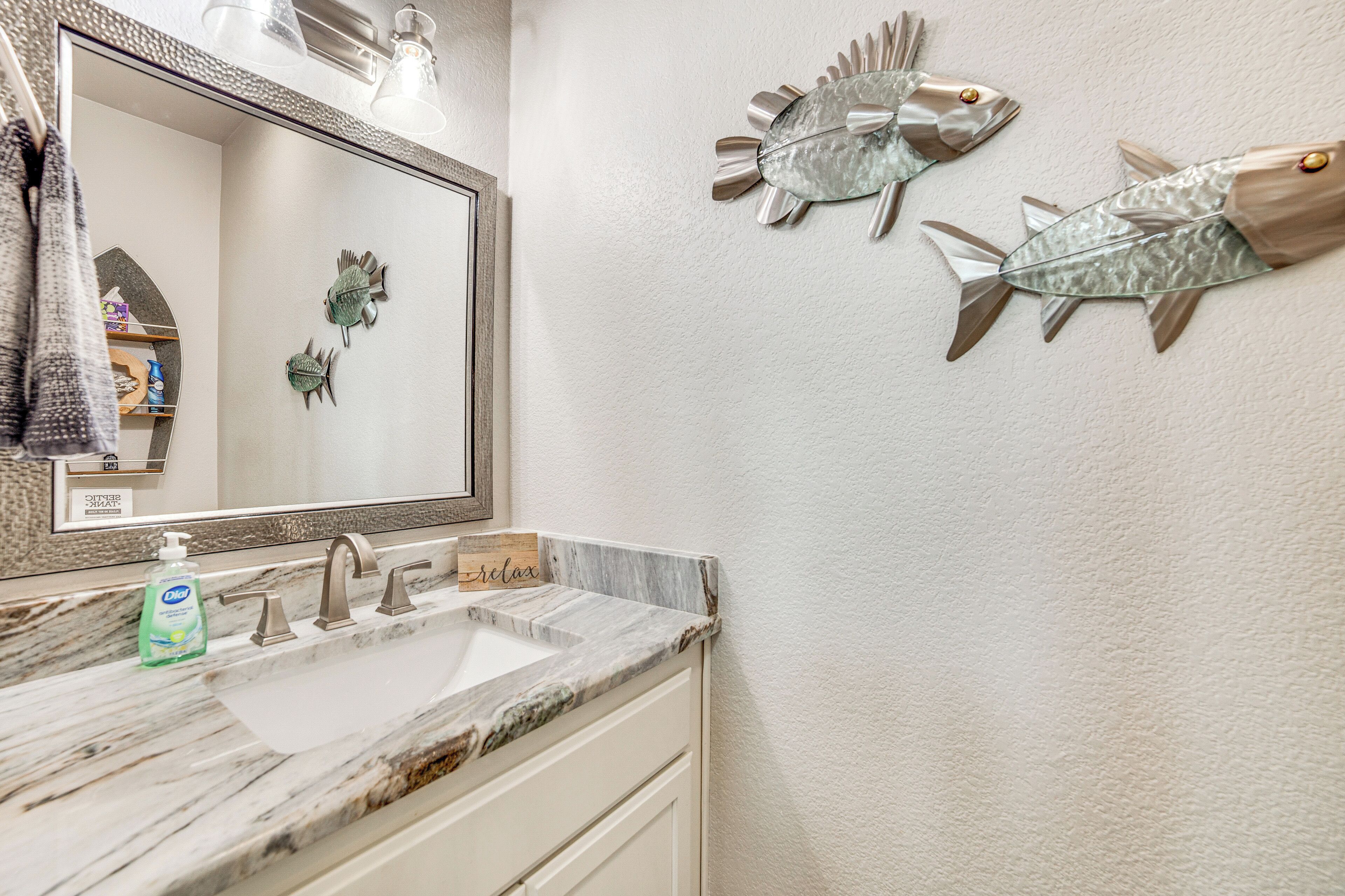 A bathroom with a marble sink, a large mirror, and decorative fish wall art.