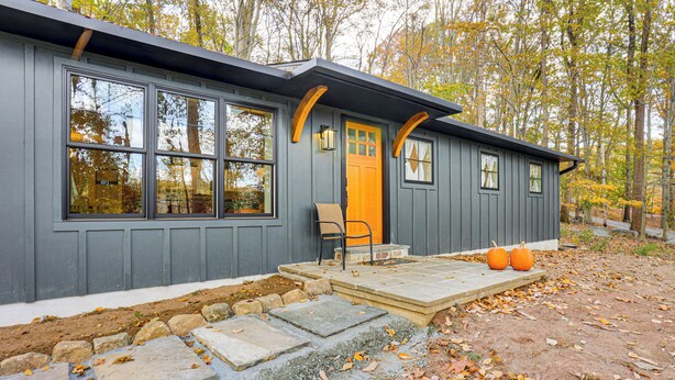 A modern house with a gray exterior, large windows, a wooden door, and a porch with steps leading to the entrance. - Serene Getaway w/ Trail Access in Chester Springs (Chester Springs)
