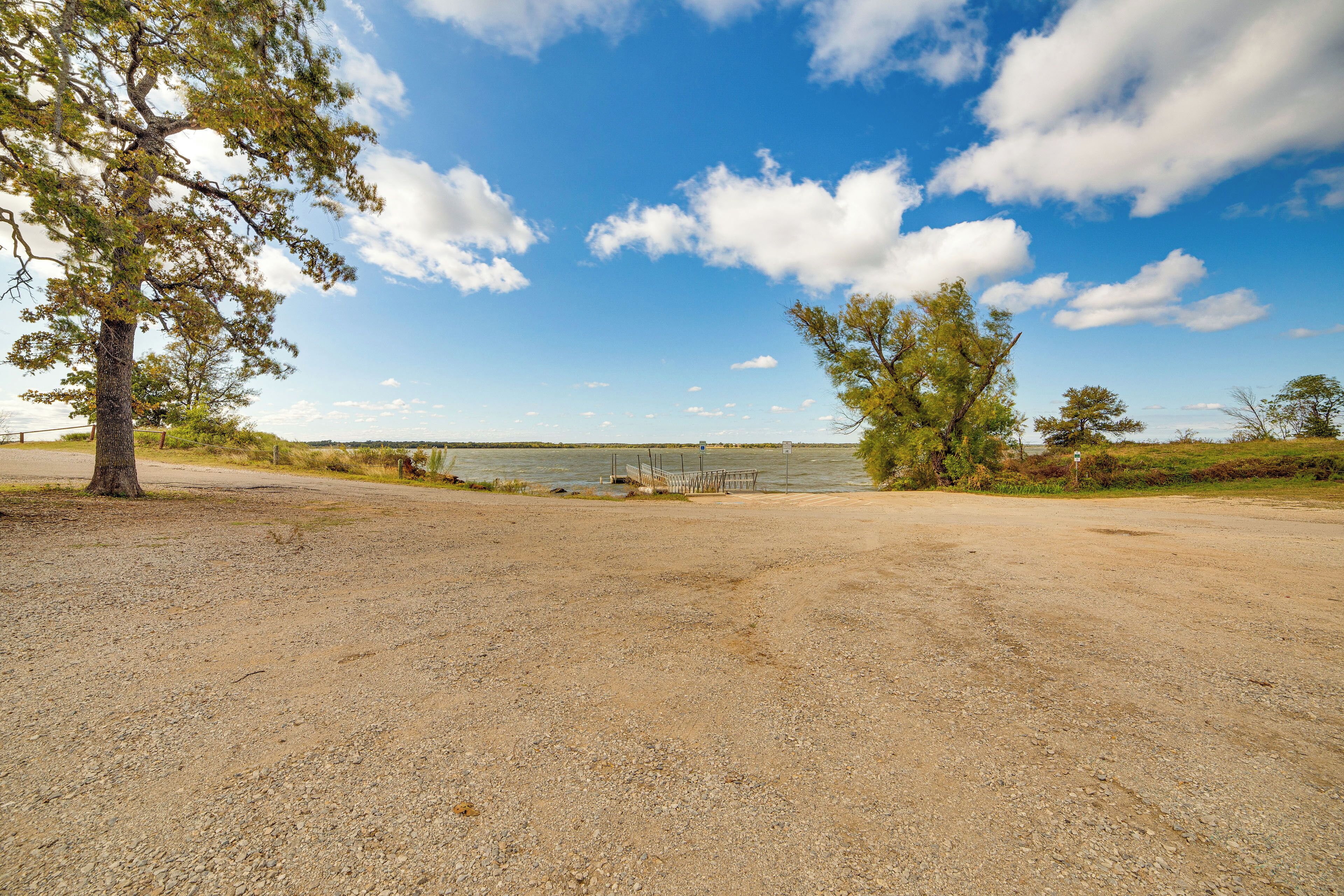 A gravel parking area with trees and a clear view of a body of water in the distance.