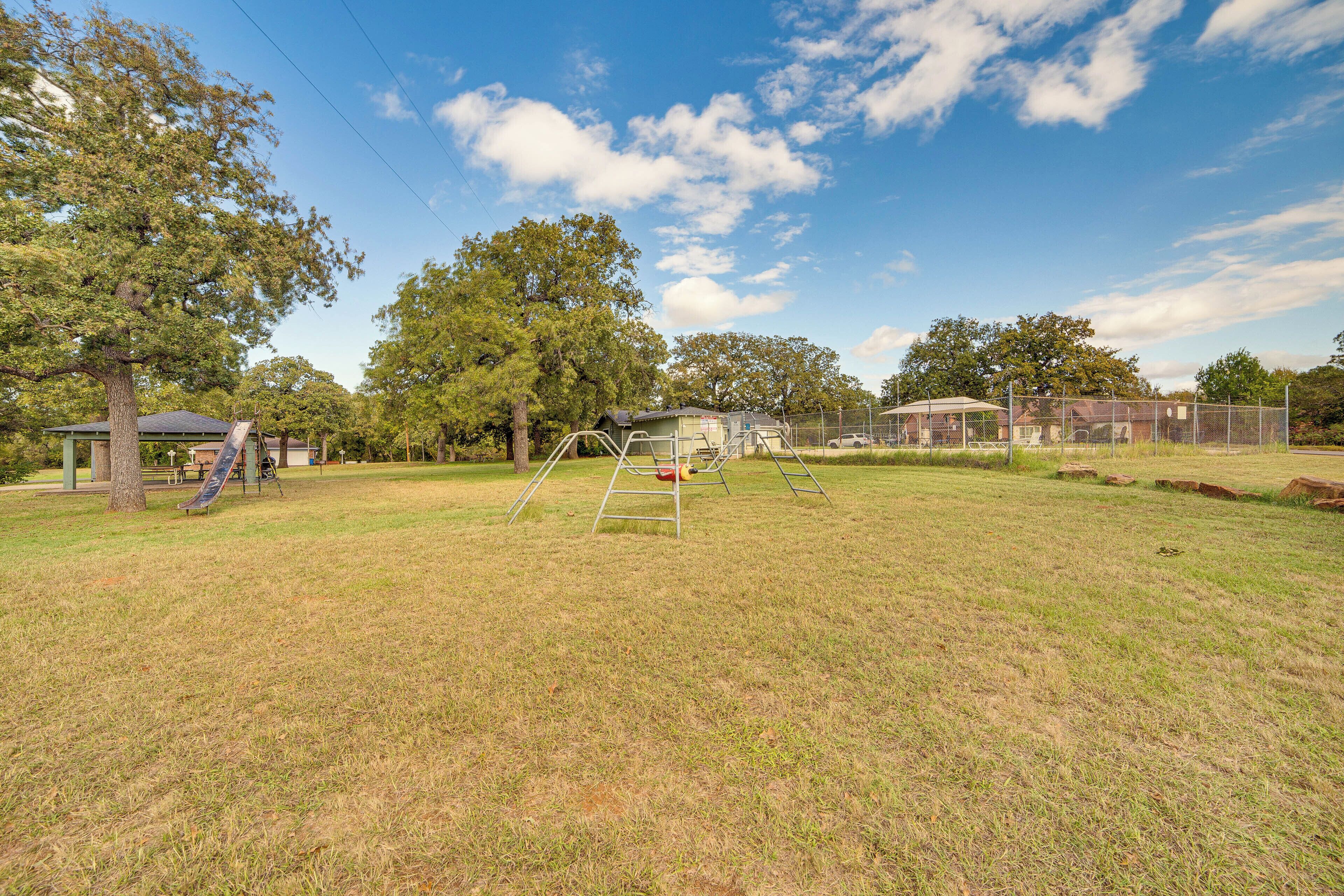 A grassy park area with playground equipment, trees, and a building in the background.