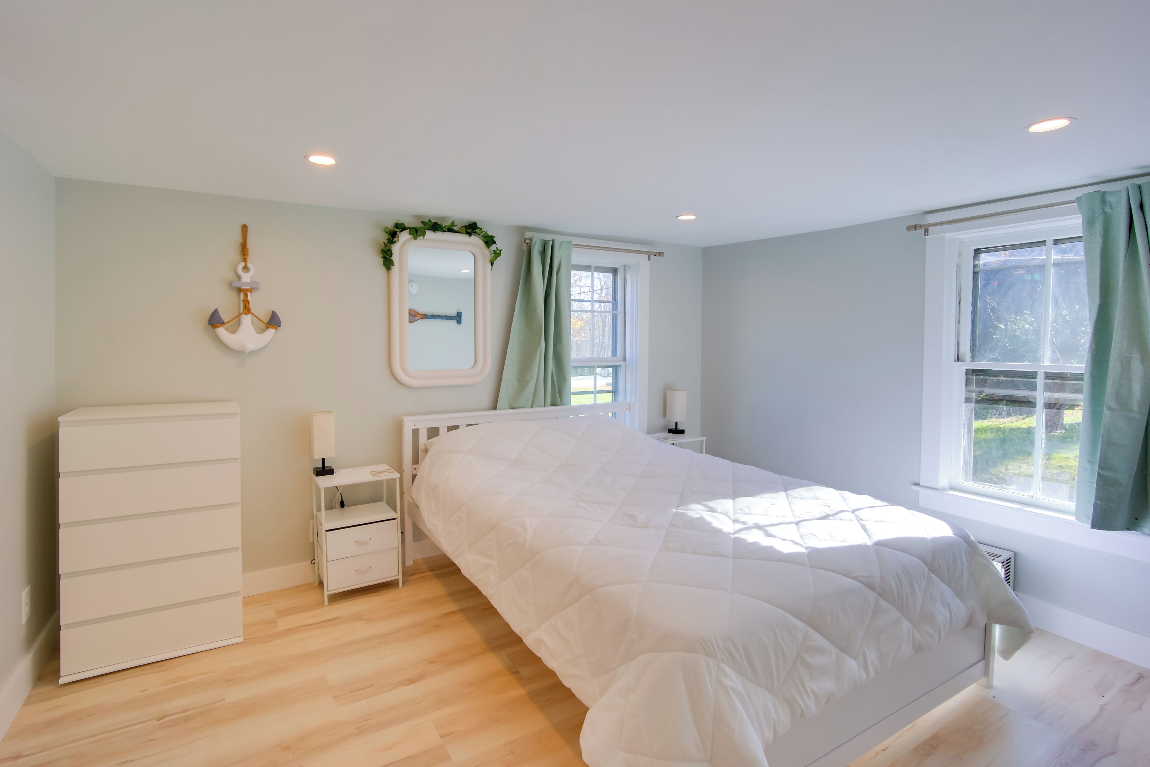 Un dormitorio con cama, cómoda, mesita de noche, espejo y ventana con cortinas.