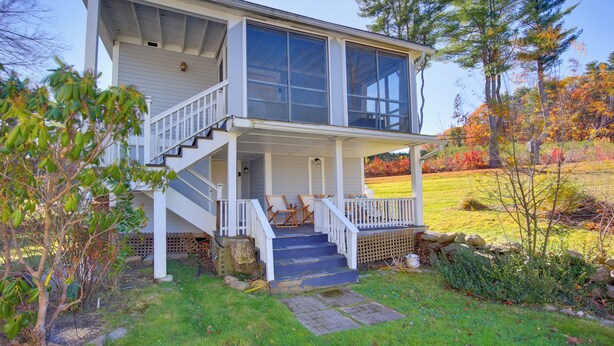 Ein zweistöckiges Haus mit verdeckter Veranda, einer Treppe, die zu der oberen Etage führt, und einem gepflegten Garten mit Bäumen und Sträuchern.