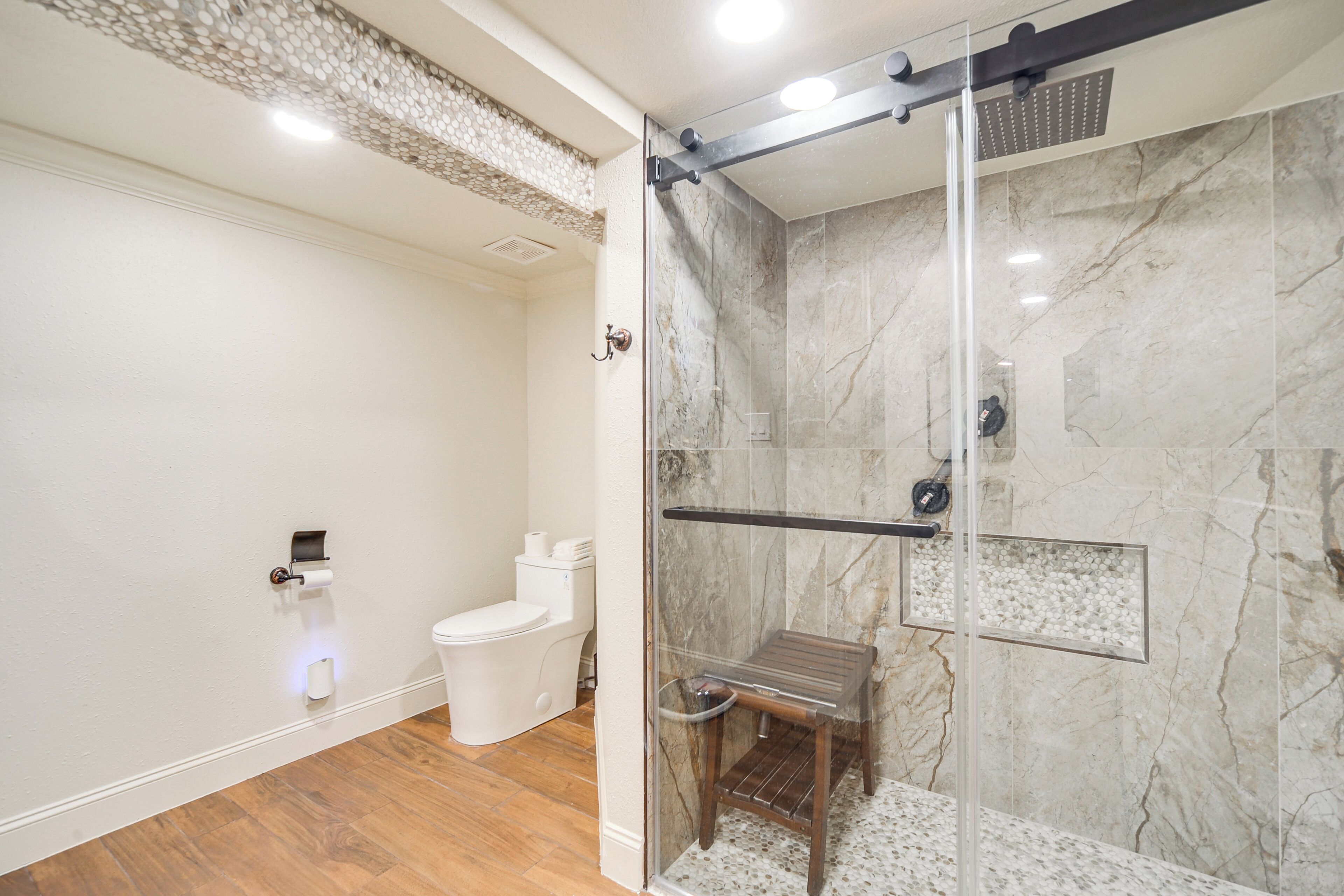 A modern bathroom with a glass-enclosed shower, a toilet, and a marble wall.