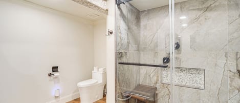 Een moderne badkamer met een douche met glazen wand, een toilet en een marmeren wand.