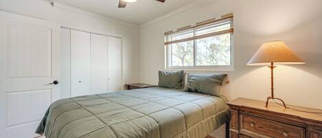 Ein Schlafzimmer mit Bett, Nachttisch, Kommode, Deckenventilator und Fenster mit Jalousien.