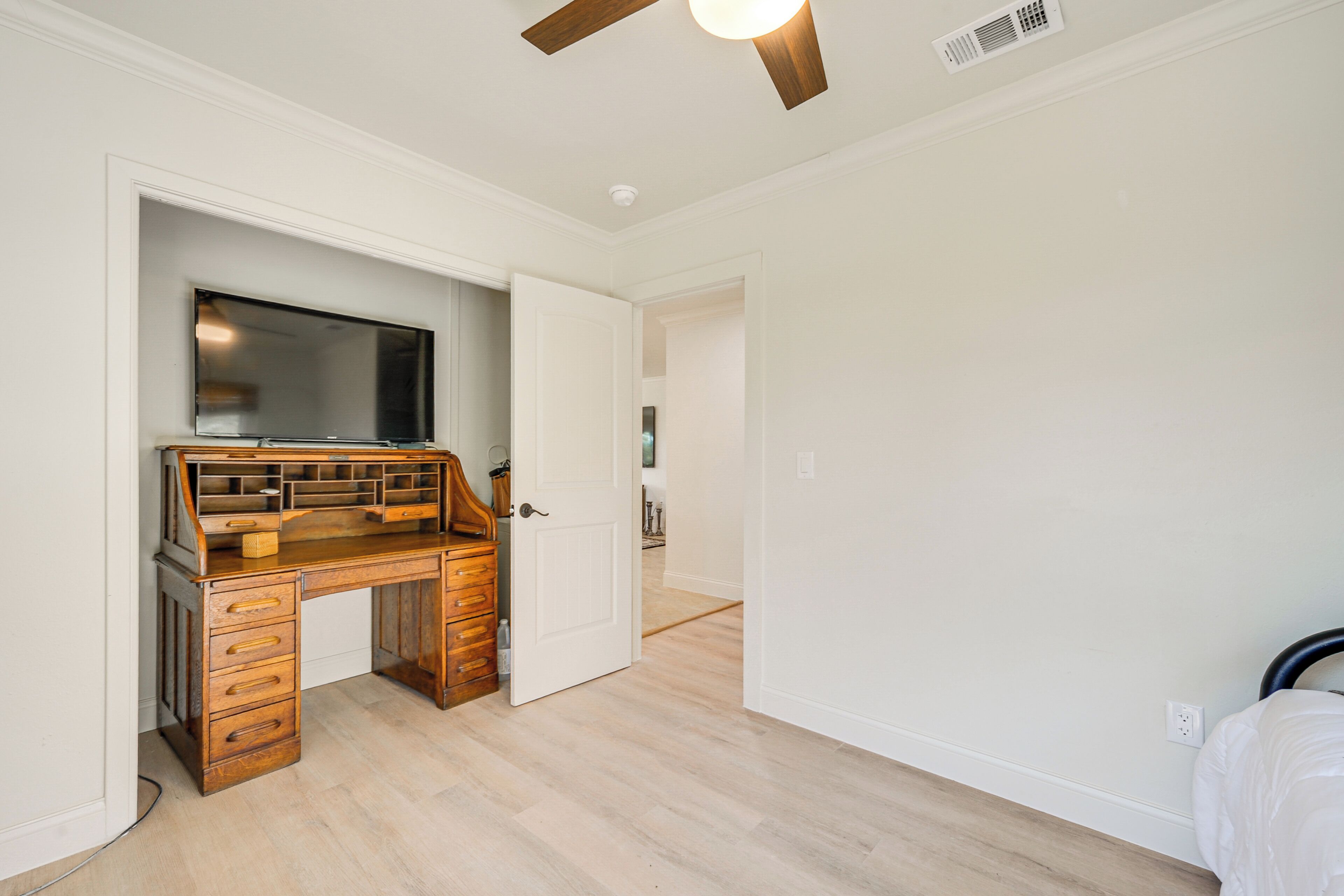 Une chambre avec un bureau en bois, un lit et un ventilateur de plafond.