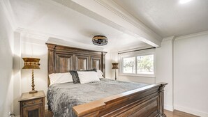 Un dormitorio con una cama de madera grande, dos mesitas de noche, una lámpara decorativa en el techo y una ventana con vistas a árboles.