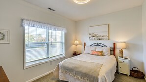 Una camera da letto con un'ampia finestra, un letto con copriletto decorato, due comodini con lampade, un'opera d'arte appesa al muro e un lampadario al soffitto.