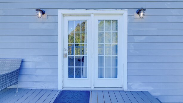 Ein Haus mit einer weißen Tür, zwei Wandleuchten und einem blauen Deck mit Fußmatte.