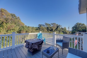 A deck with outdoor furniture, a covered grill, and a view of trees and a vehicle in the background. - Walk to Fishing Pier, Newport Home w/ Deck! (Newport)
