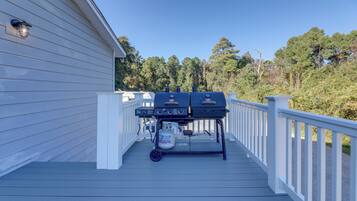 A deck with a barbecue grill and propane tank, surrounded by white railings and a house with siding.