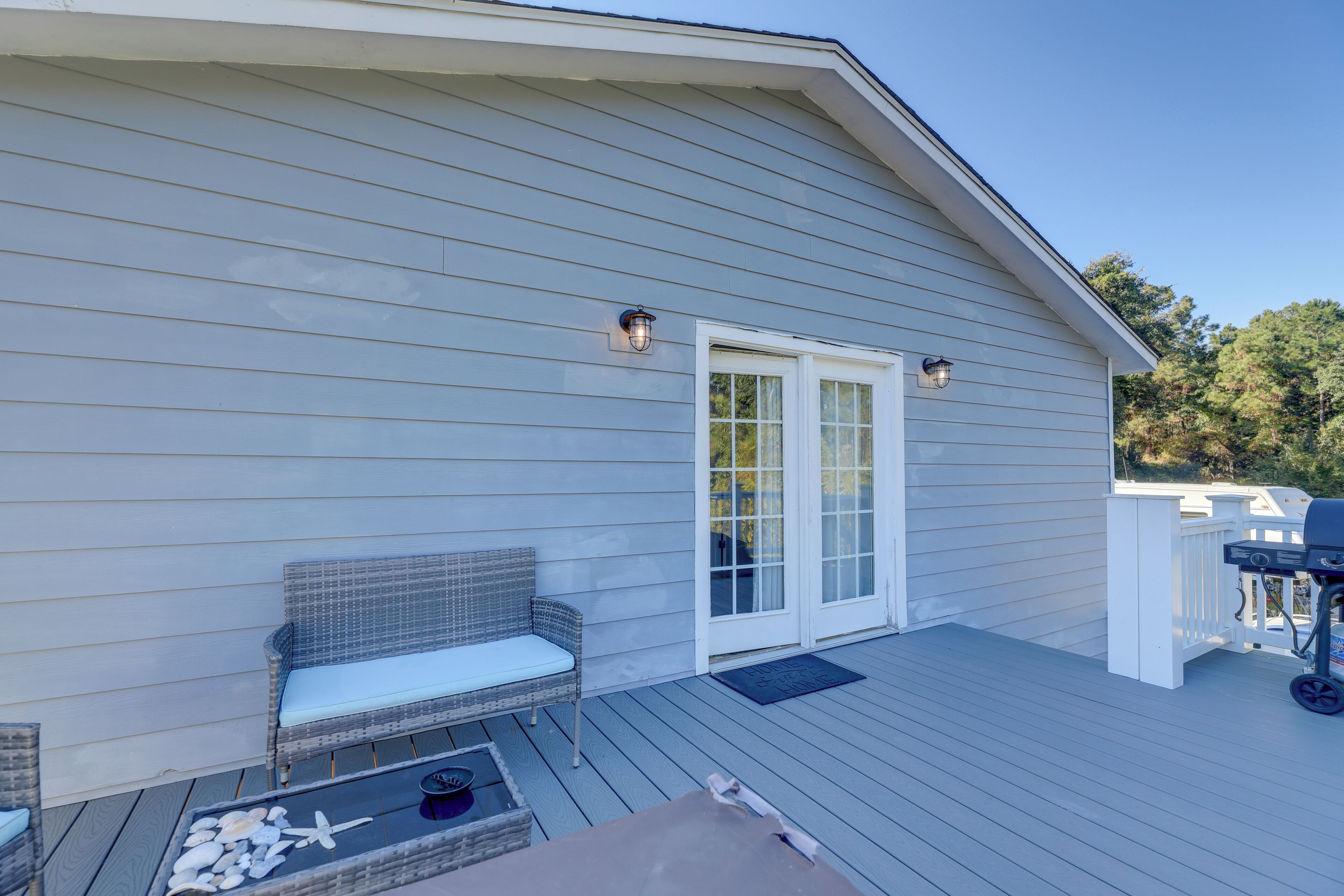 A covered deck with a wicker sofa, a barbecue grill, and a small table with decorative items.