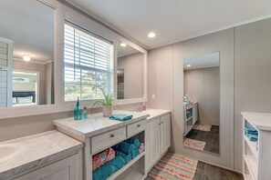 A modern bathroom with a large mirror, a sink, and a window. There are towels and a plant on the counter. - 'coastal Cozy' - Newport Home w/ Private Hot Tub (Newport)