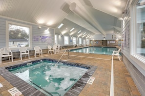 Una piscina interior con agua cristalina, rodeada de sillones de descanso y un suelo de baldosas.